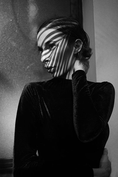 a dramatic black and white portrait of a young woman with a plant leaves shadow casted on her face