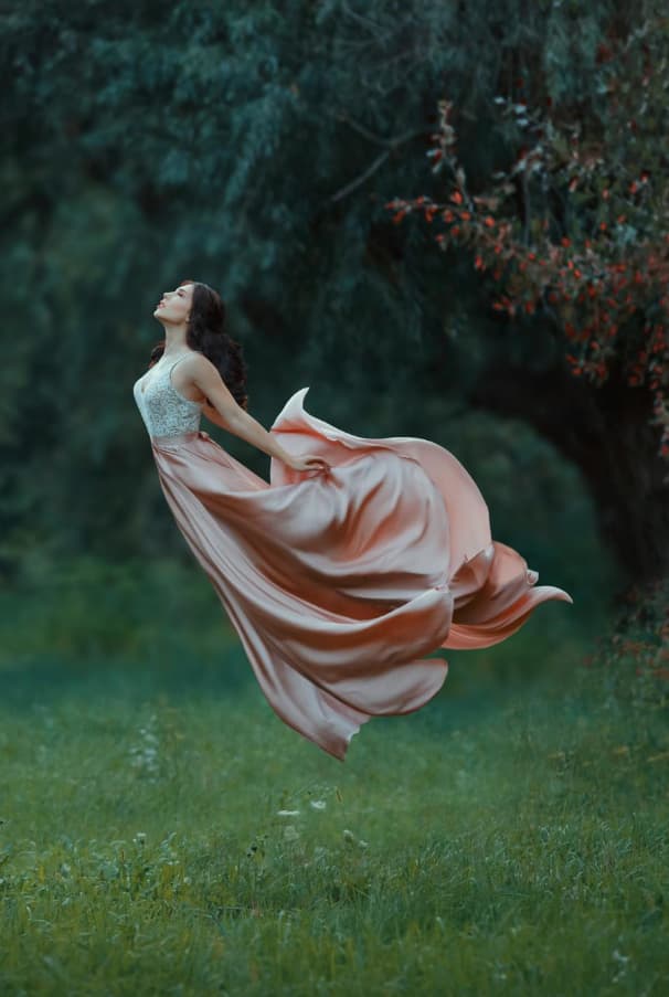 Girl wearing a long gown and floating in forest